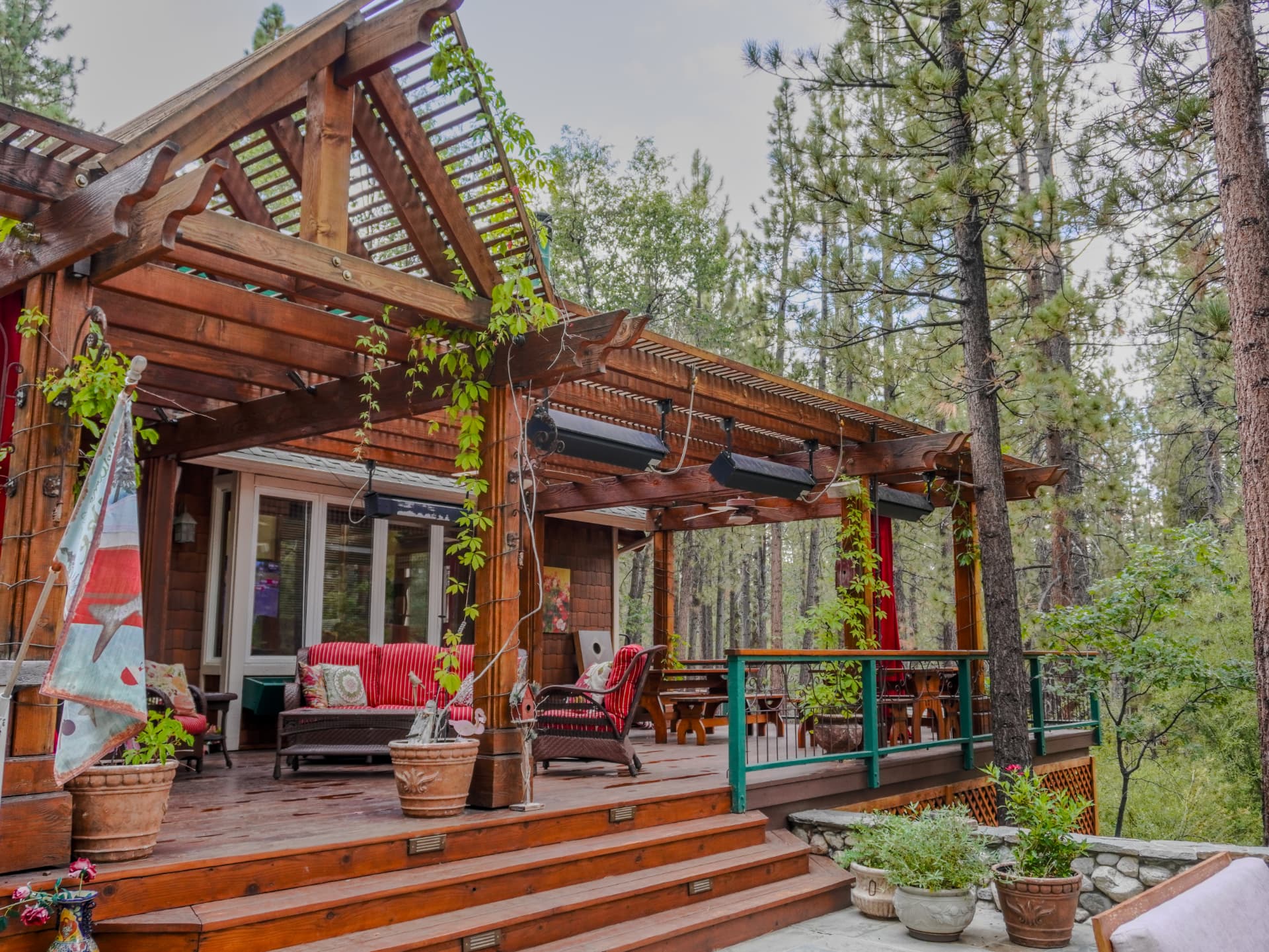 Covered redwood pergola deck with timber beams and vine-wrapped posts at 42388 Switzerland Drive, surrounded by tall pines